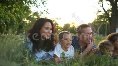 夫妻和三个孩子在日落时分躺在草地上，暑假，快乐的孩子和他们的父母
